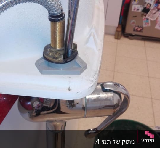 כיור עם ברז וצינורות מתכת, דלי ירוק על הרצפה